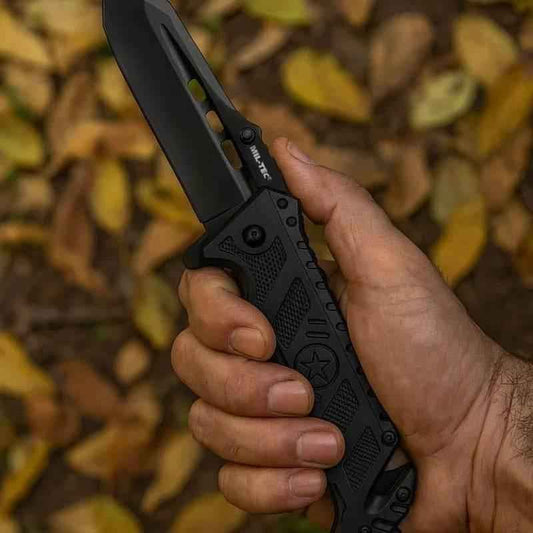 Navaja MIL-TEC negra en la mano, empuñadura texturizada y protector